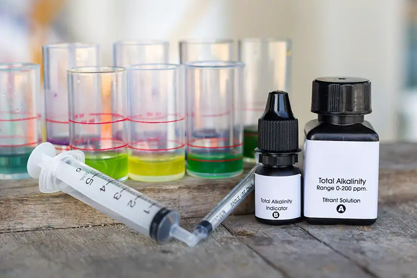 An alkalinity test kit mixes chemicals in a test tube with aquarium water producing a color reaction that can be compared to a measurement chart.